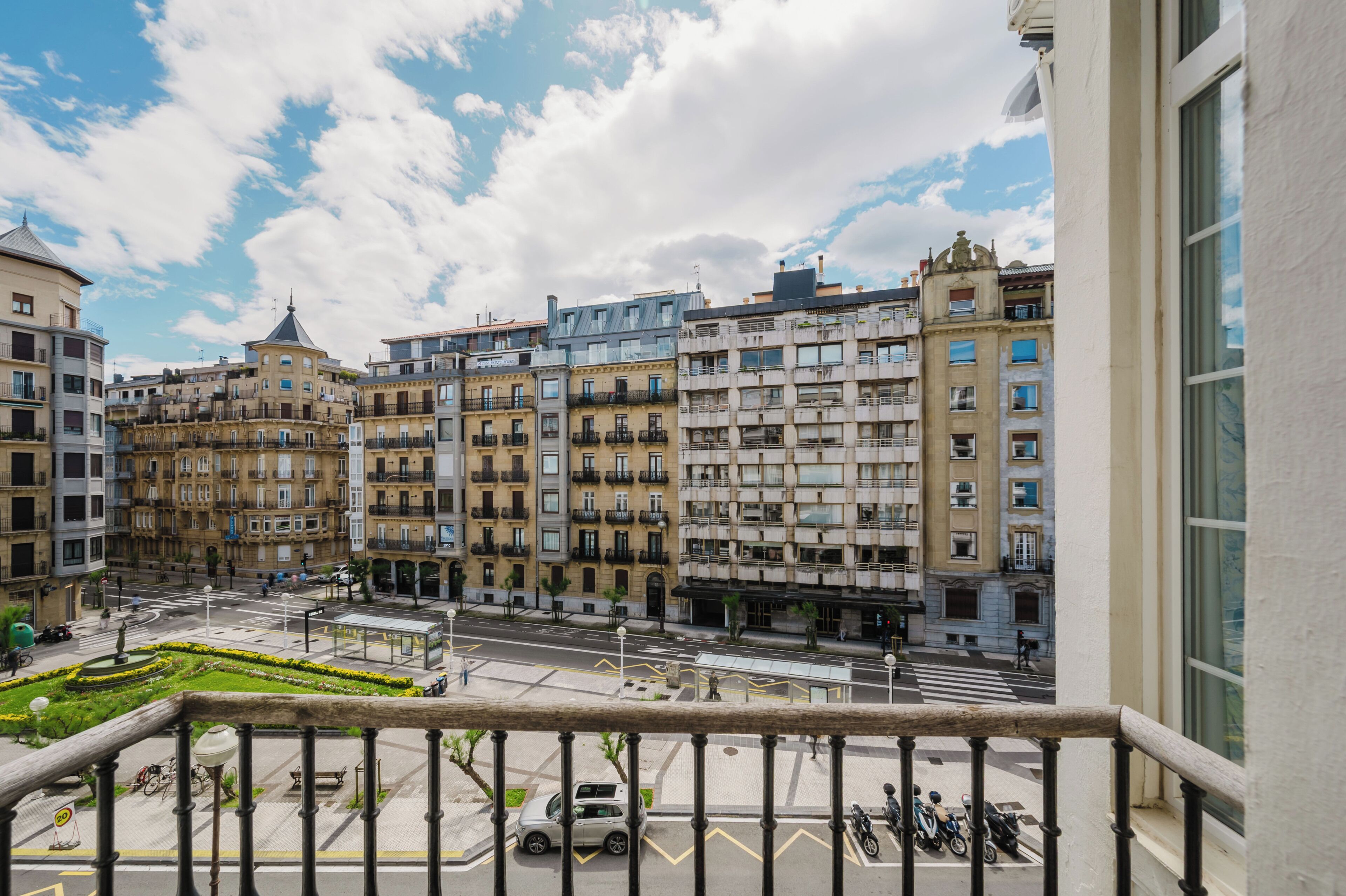 Un balcon offrant une vue sur le paysage urbain, avec des immeubles à plusieurs étages et une rue où circule un tramway.