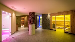 A modern interior with a central pillar, wooden panel walls, and a seating area with yellow lighting. - Hotel Mühlener Hof (Campo Tures)
