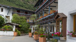 A traditional chalet with a wooden balcony, flower boxes, and a mountain backdrop. - Hotel Mühlener Hof (Campo Tures)
