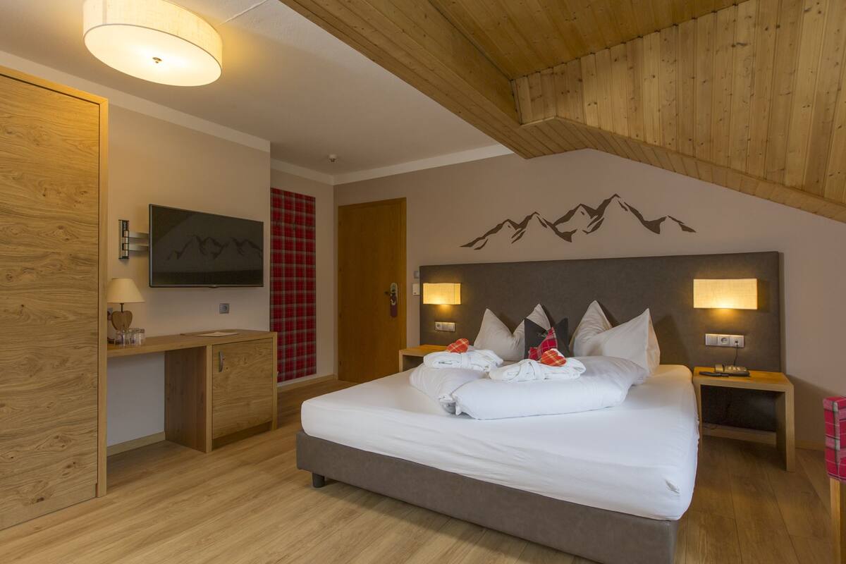 Quarto com cama, mesas de cabeceira, televisão e teto de madeira.