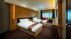 A hotel room with two beds, a desk, and a window with curtains.