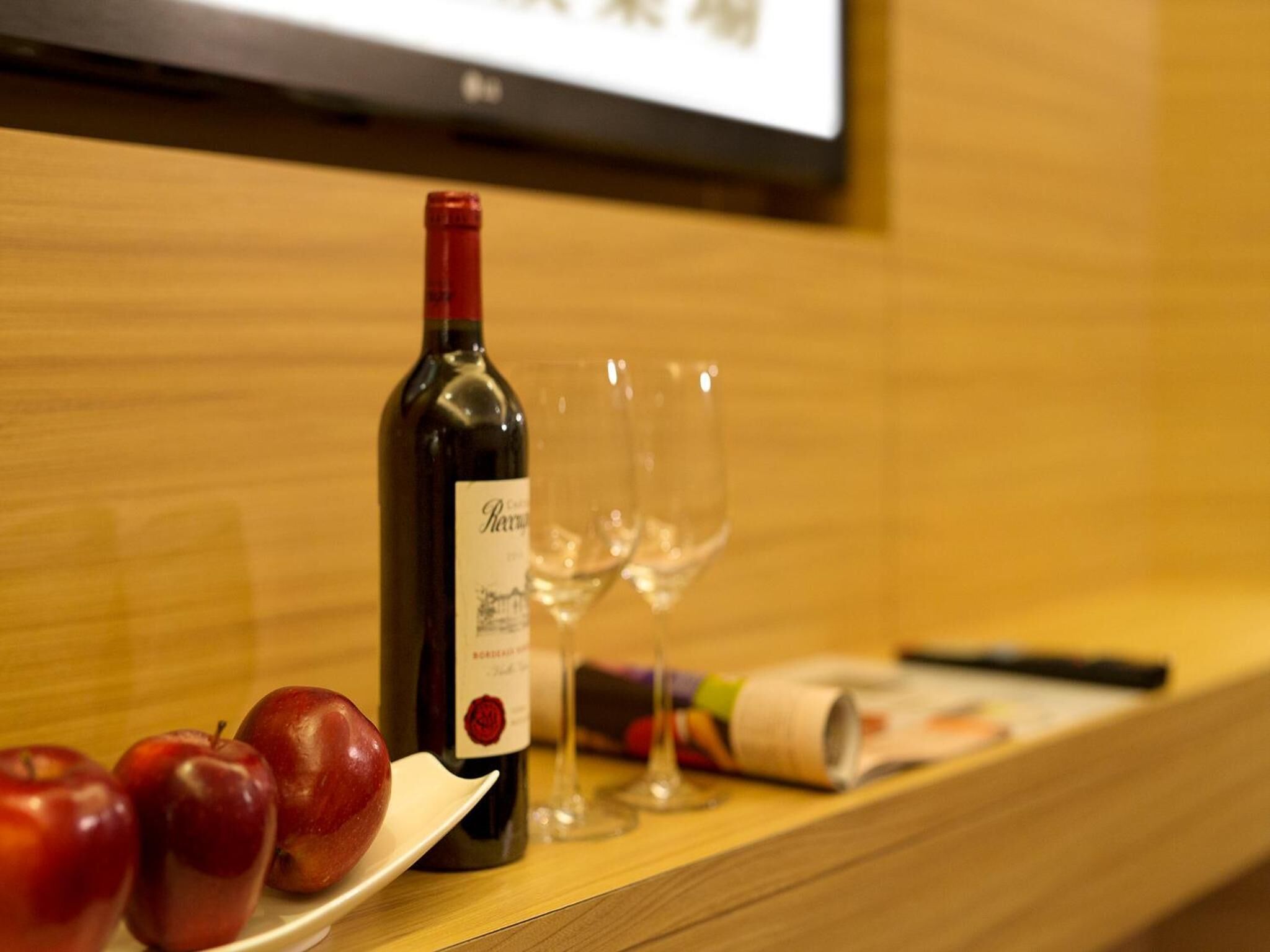 A bottle of wine, two empty wine glasses, and a plate with apples on a wooden counter.