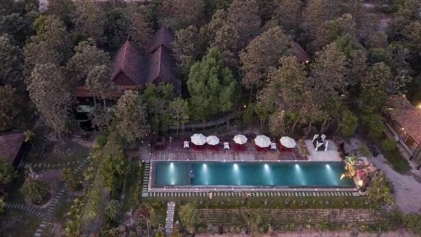 Ett flygbildsbild av ett semesterområde med en swimmingpool, omgivet av träd och några få byggnader.