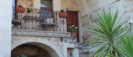 A courtyard with a stone archway, potted plants, and a balcony with wrought iron railings.