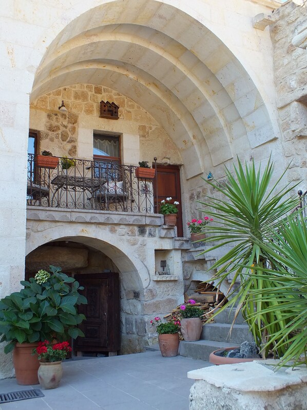 A courtyard with a stone archway, potted plants, and a balcony with wrought iron railings.