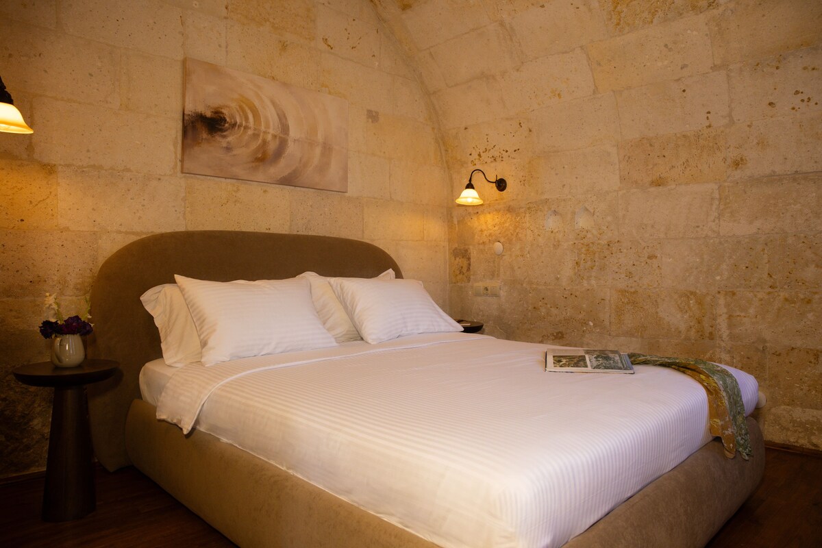 Una cama con ropa blanca en una habitación con paredes de piedra y una única lámpara de pared.