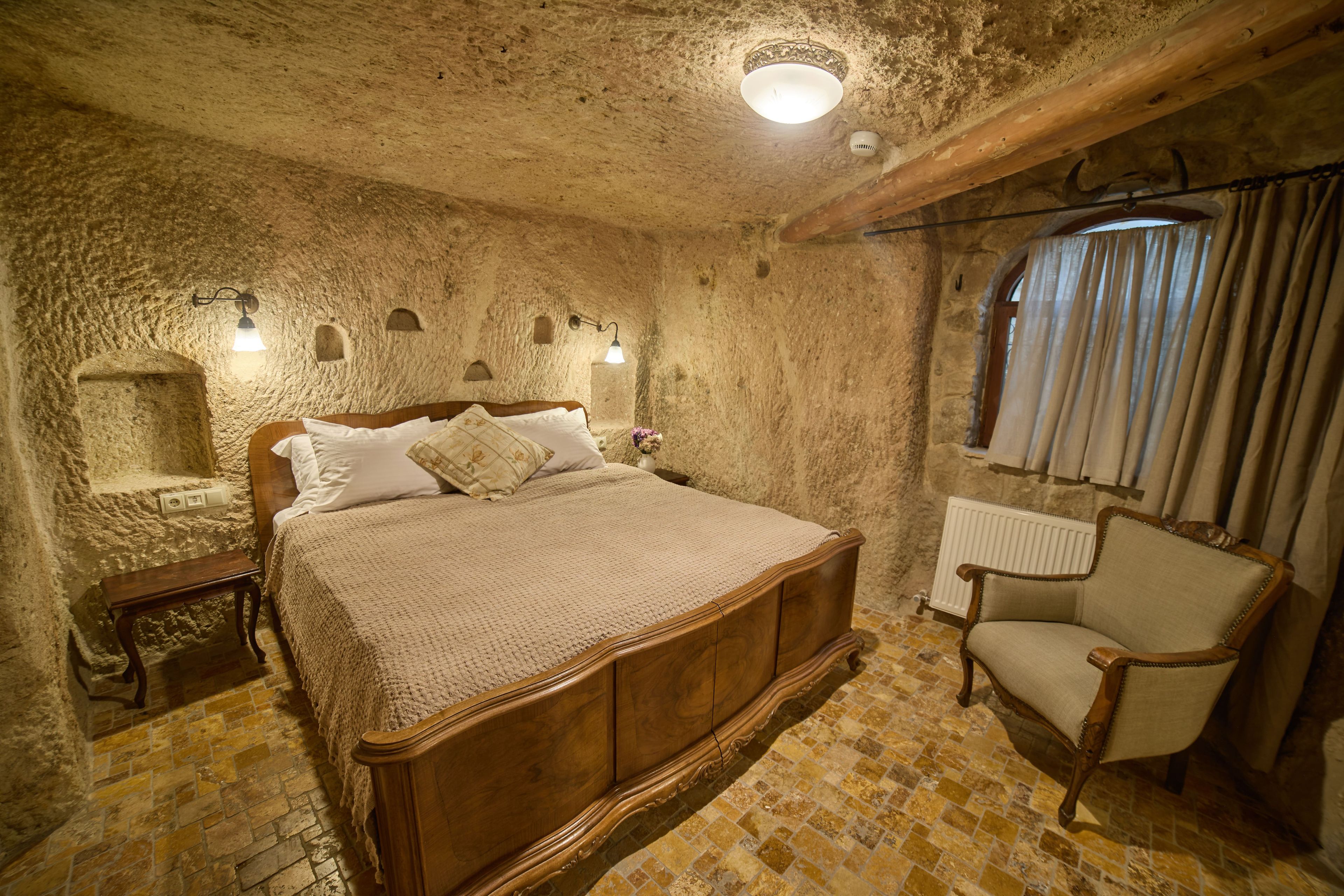 Un dormitorio con pared de piedra, cama de madera, una silla y un radiador.