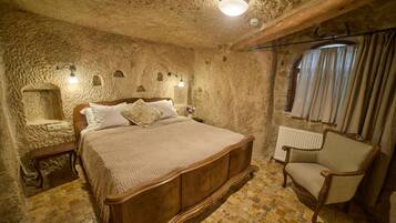 Un dormitorio con pared de piedra, cama de madera, una silla y un radiador.