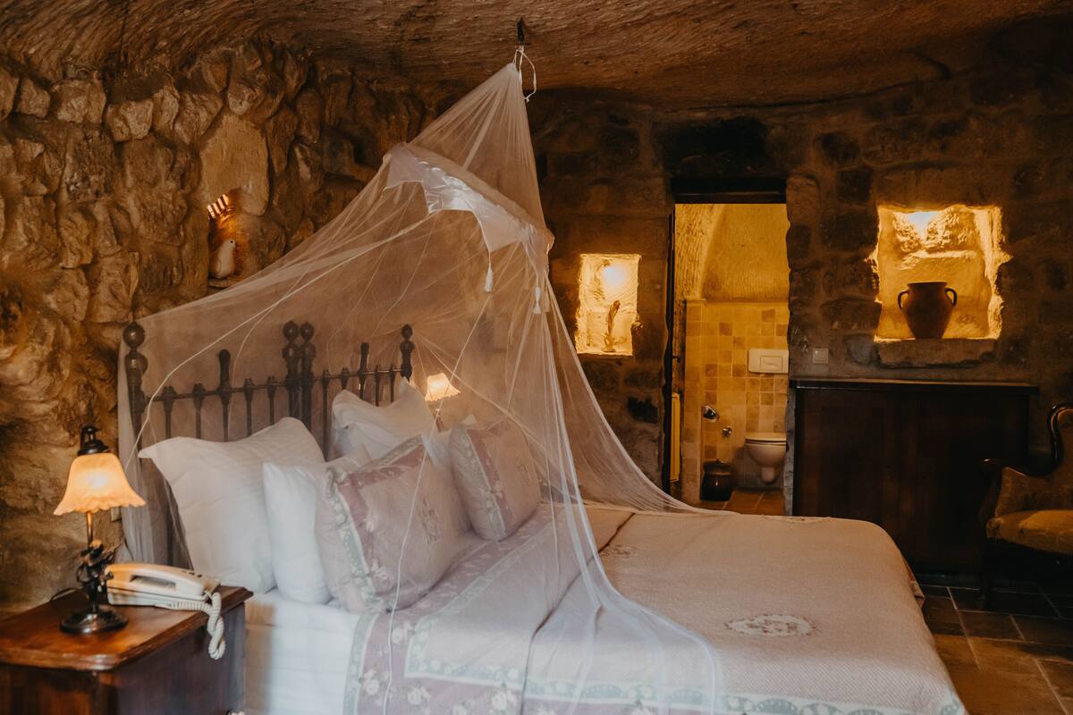 Un dormitorio con paredes de piedra, una cama con dosel, una lámpara de noche y una mesita con teléfono.