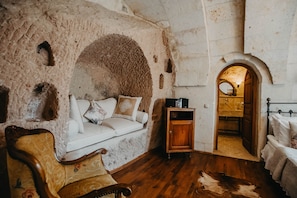 A rustic room with a stone wall, a wooden cabinet, a white sofa, a wooden chair, and a cowhide rug.