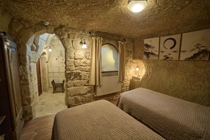 A rustic room with stone walls, a wooden door, a bench, a bed, and a wall with artwork.