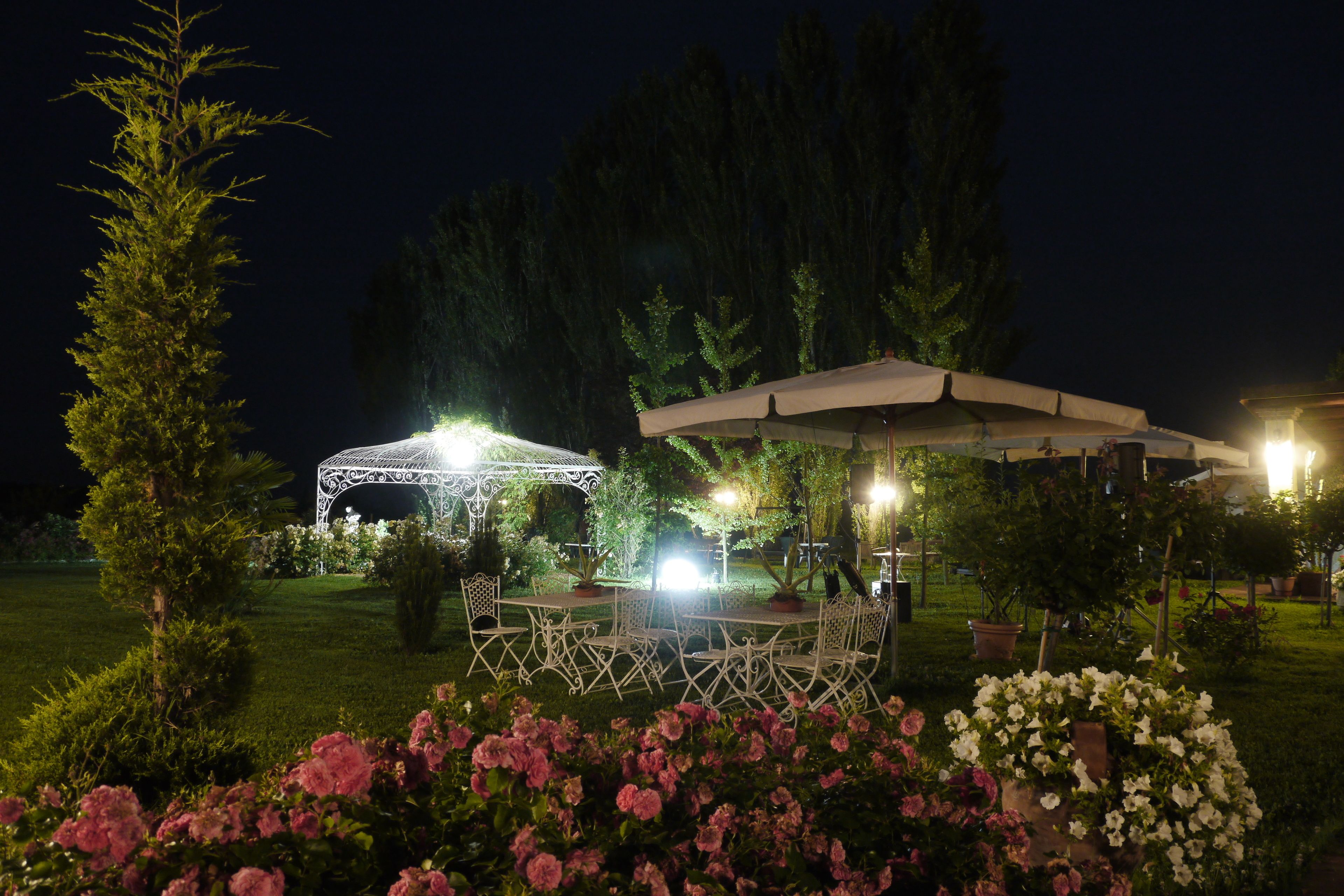Zona de jardí exterior amb una gespa de metall blanc, una taula coberta i seients, i diversos testos amb plantes i flors.