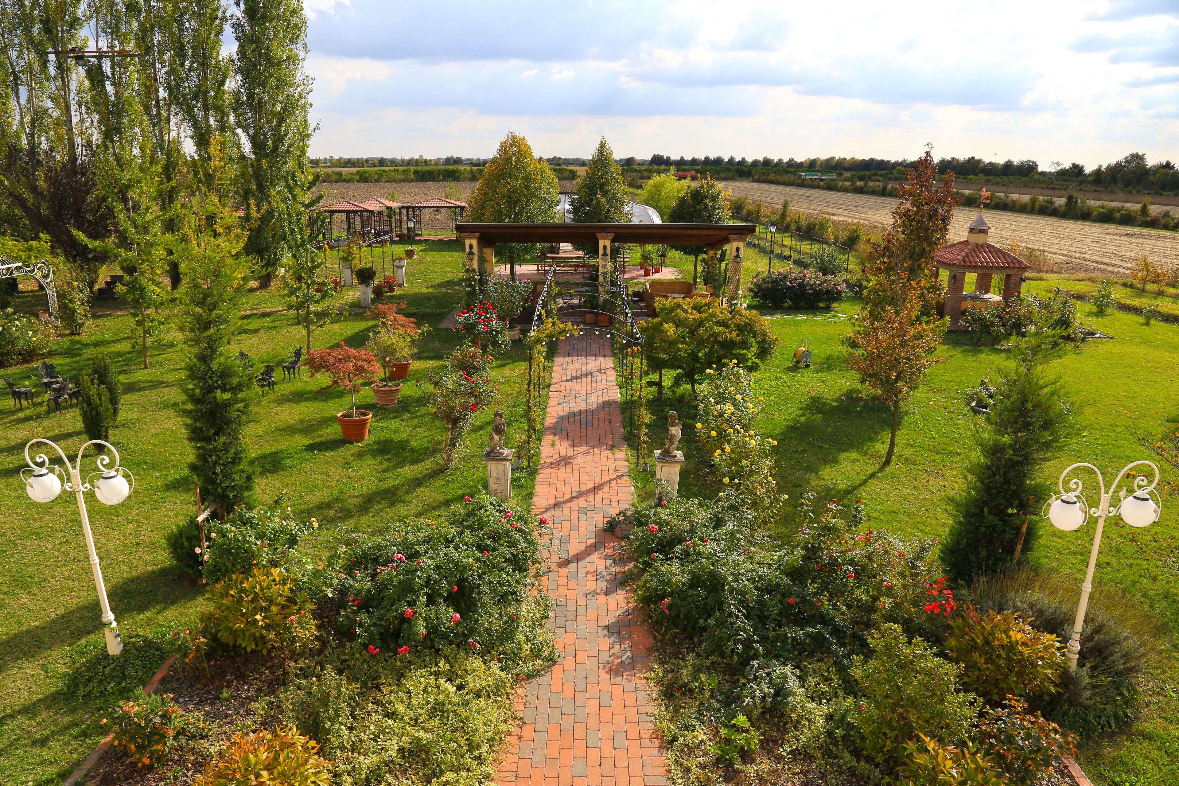 A garden with a central pathway leading to a gazebo, surrounded by various plants and trees.