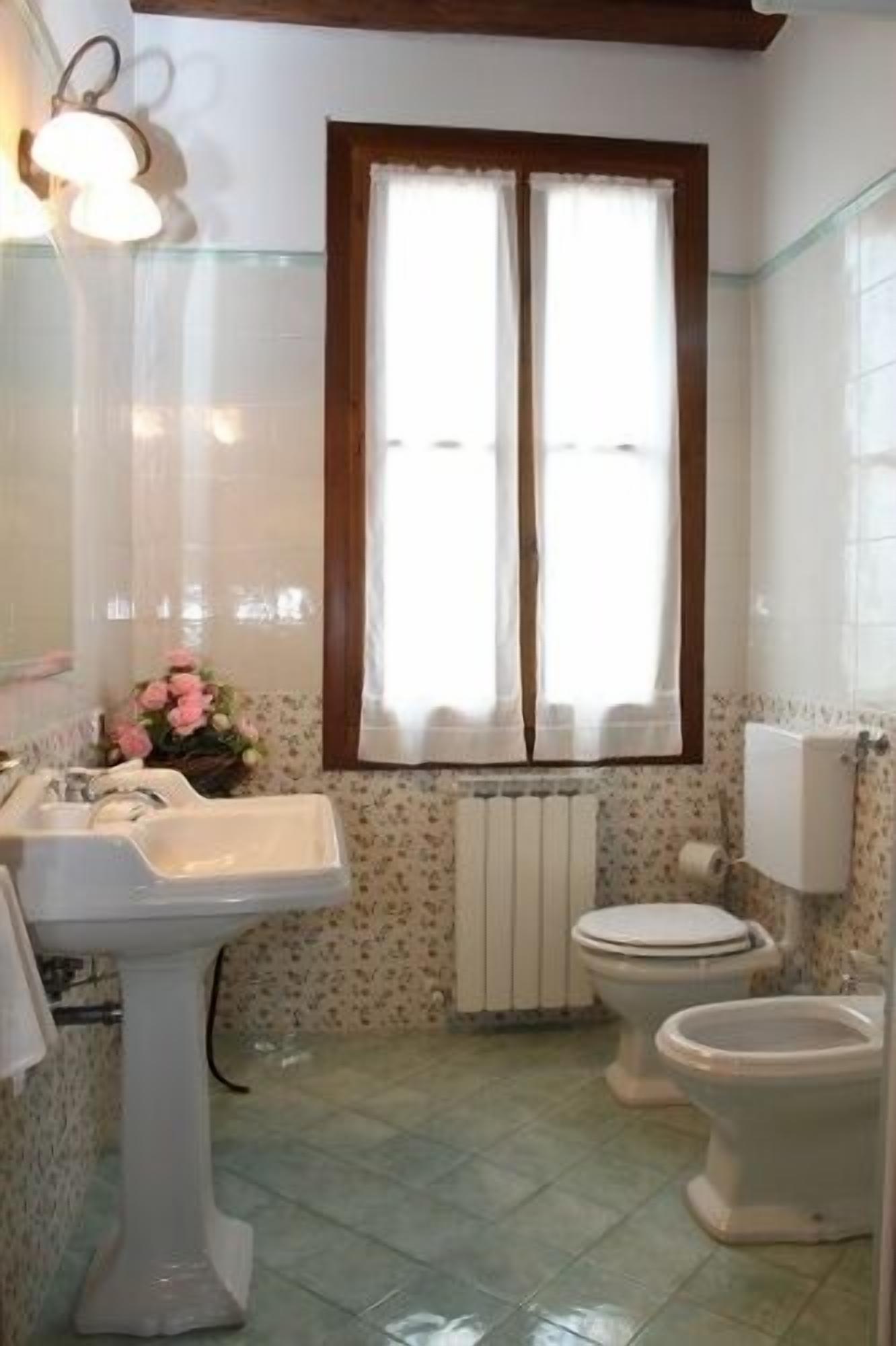 A bathroom with a sink, two toilets, a radiator, and a window with curtains.