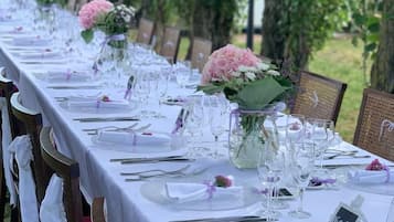 Ein langer Esstisch im Freien, gedeckt mit weißen Tischdecken, Gläsern und floralen Tischdekorationen.