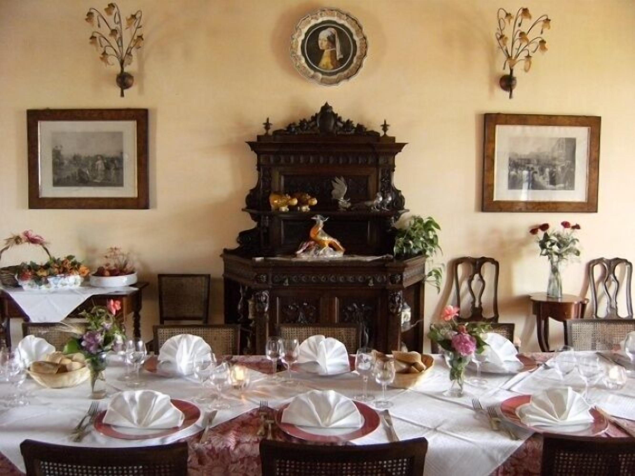A dining room with a large ornate wooden cabinet, framed pictures on the walls, and a table set for a meal.