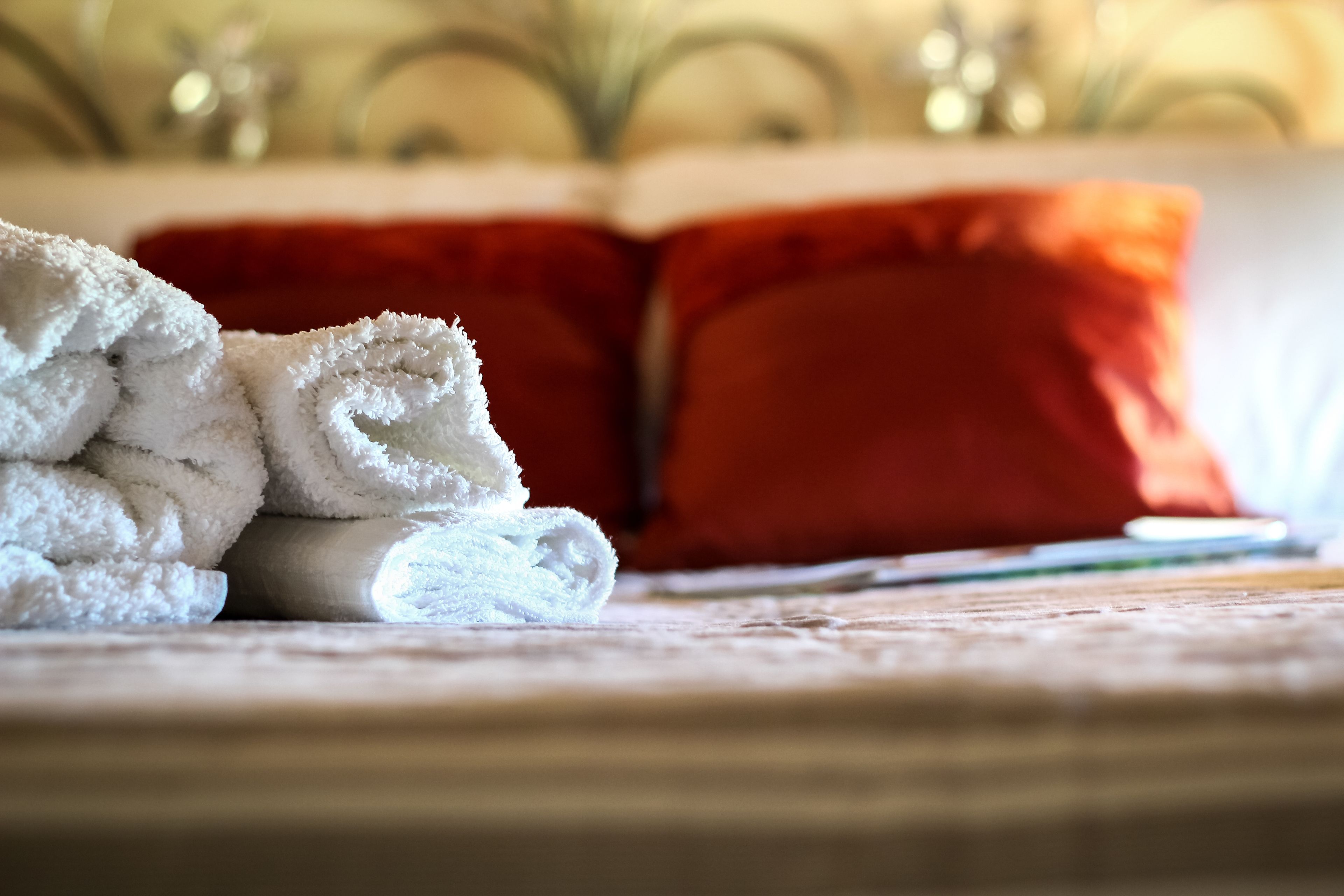 Ein Stapel weißer Handtücher auf einem Bett mit roten Kissen.