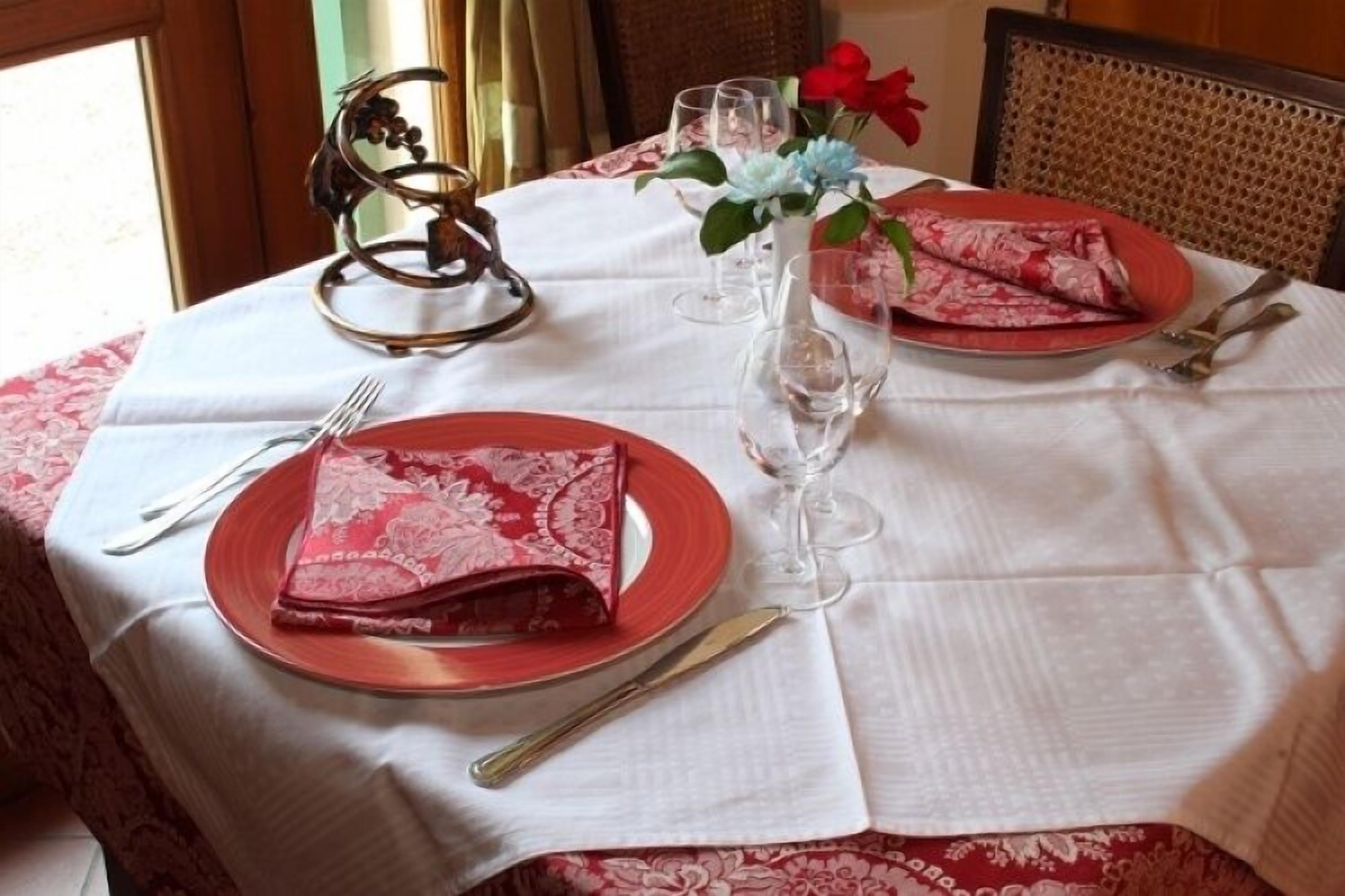 Une table à manger dressée avec des assiettes rouges, une serviette pliée, un verre à vin et des couverts.