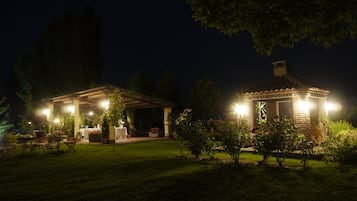 Ein gut beleuchteter Außenbereich mit Terrasse, überdachter Sitzgruppe und einem kleinen Gebäude mit Schornstein.
