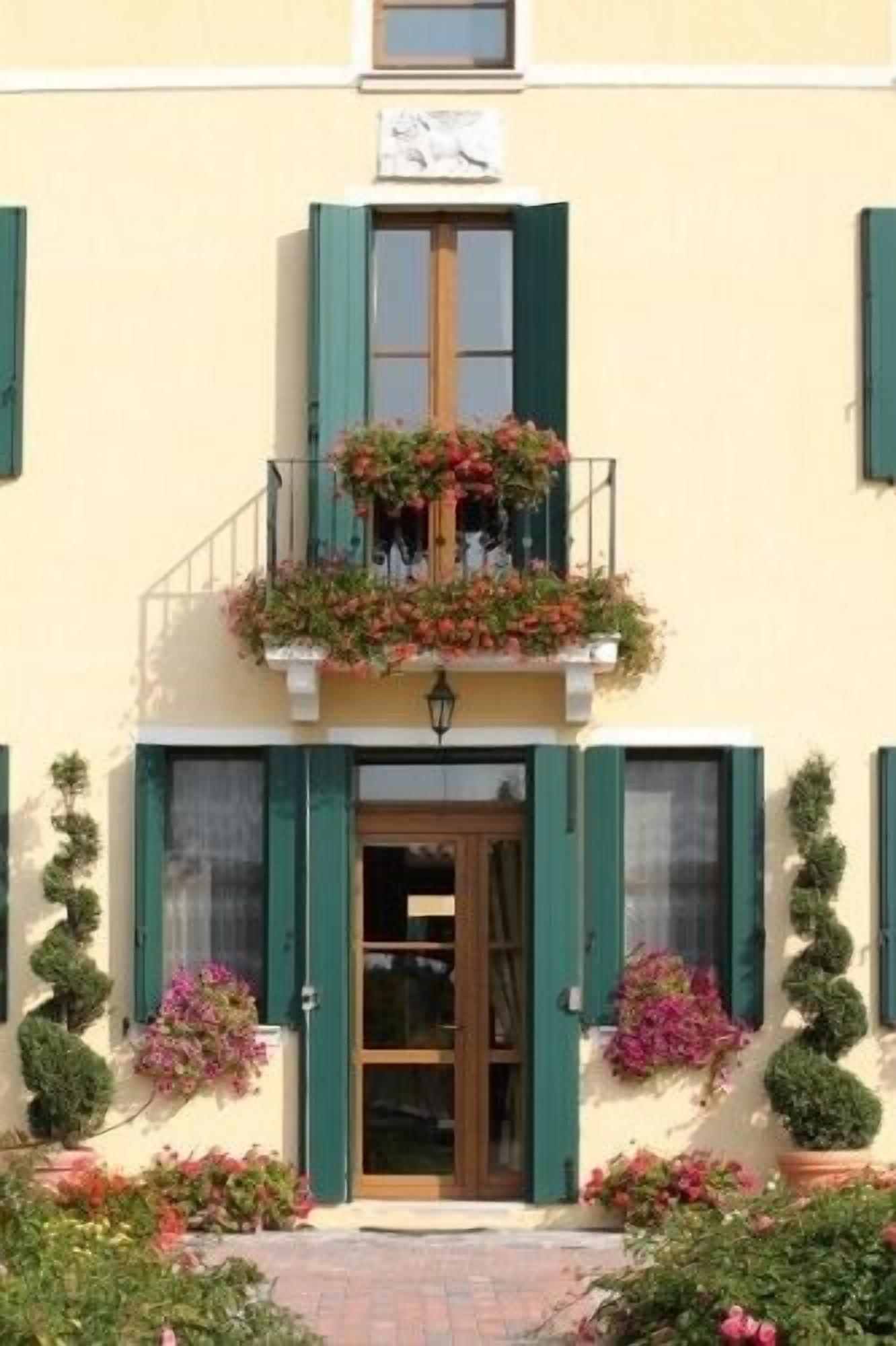 Un edificio con balcón decorado con flores, una puerta de madera y contraventanas verdes.