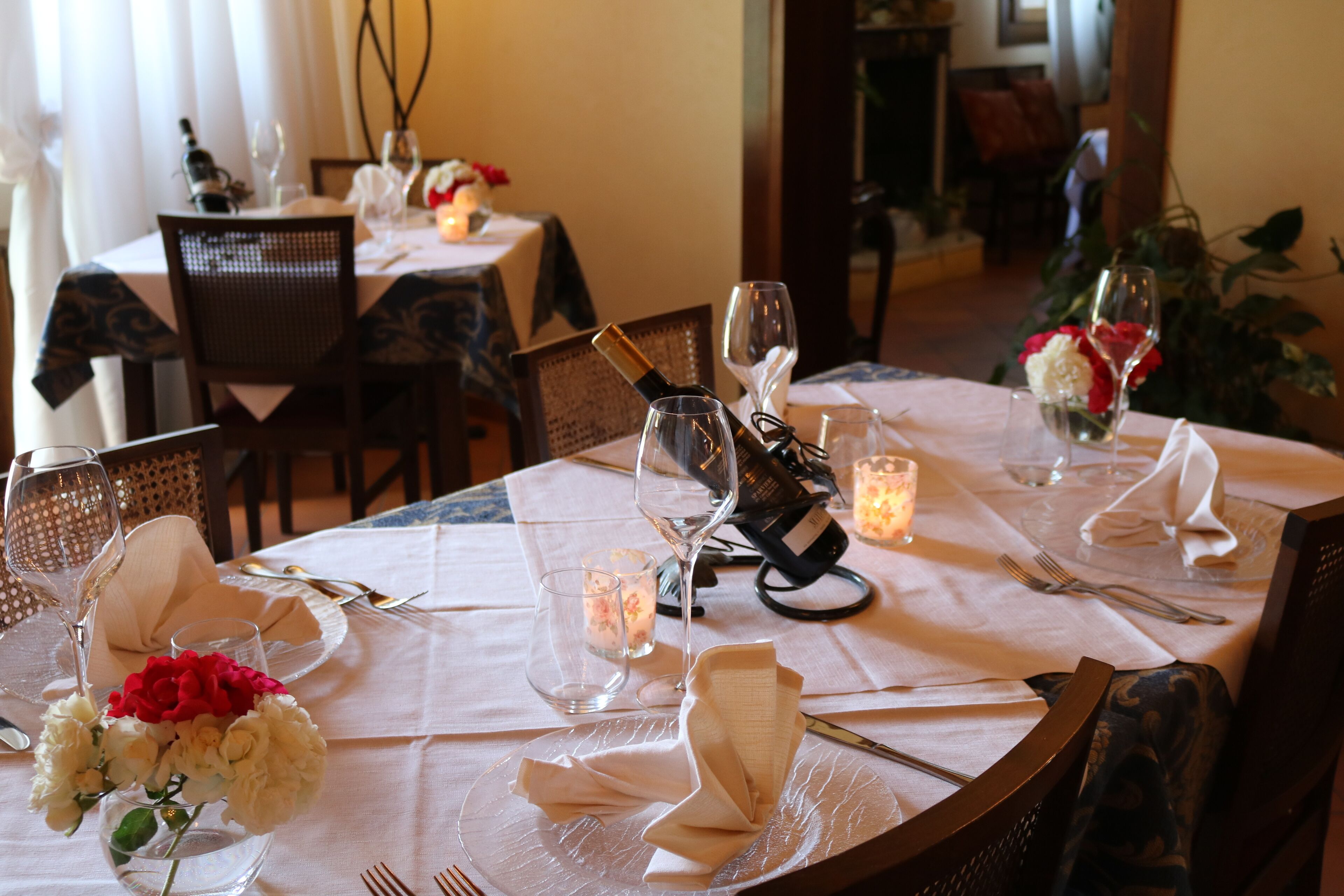 A dining table set with white tablecloth, clear glassware, and a bottle of wine.