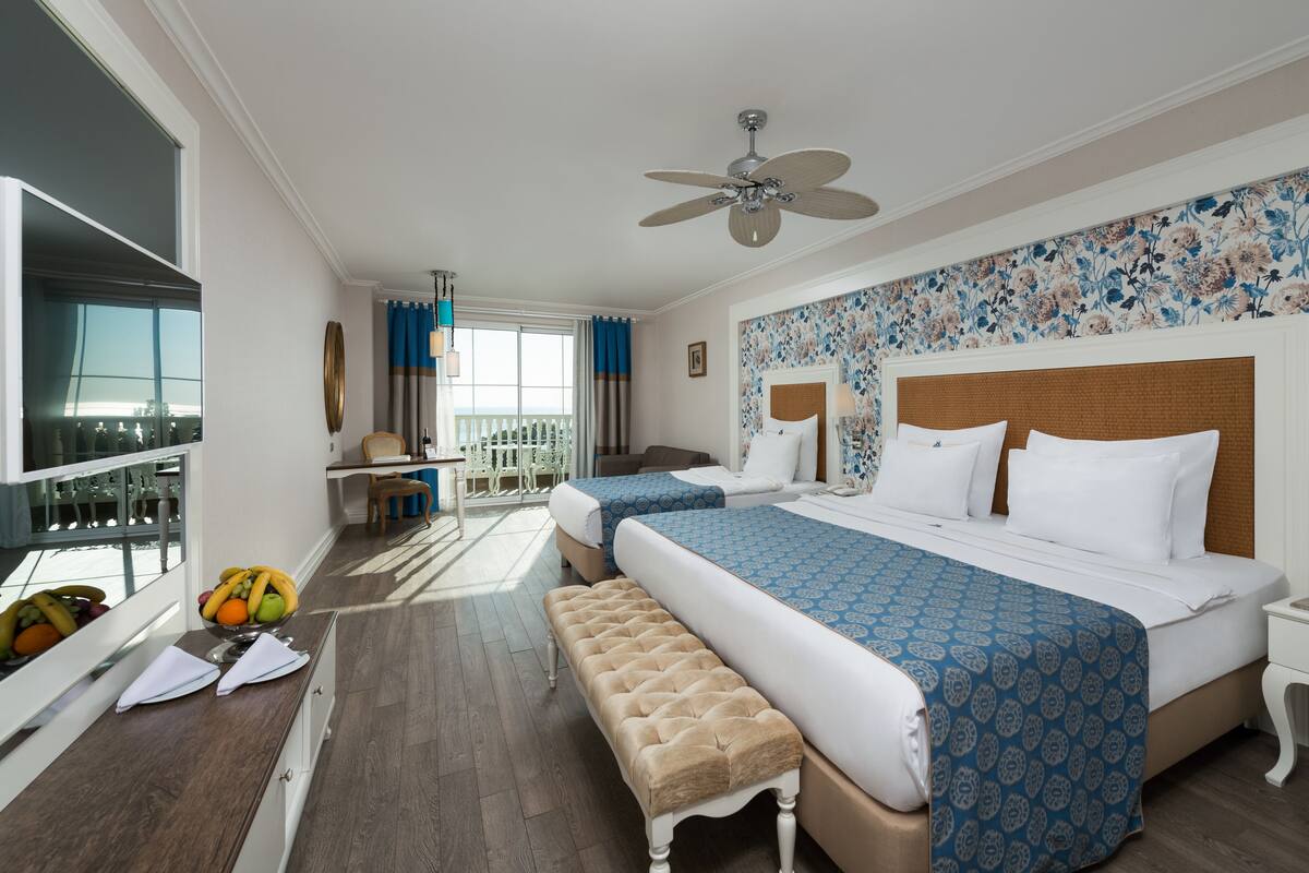A hotel room with two beds, a balcony, a dining area, and a view of the sea.