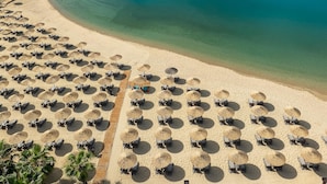 An aerial view of a beach with rows of sun loungers and umbrellas, a pier extending into the water, and a yacht in the distance. - Rubi Platinum Spa Resort & Suites - All Inclusive (Alanya)