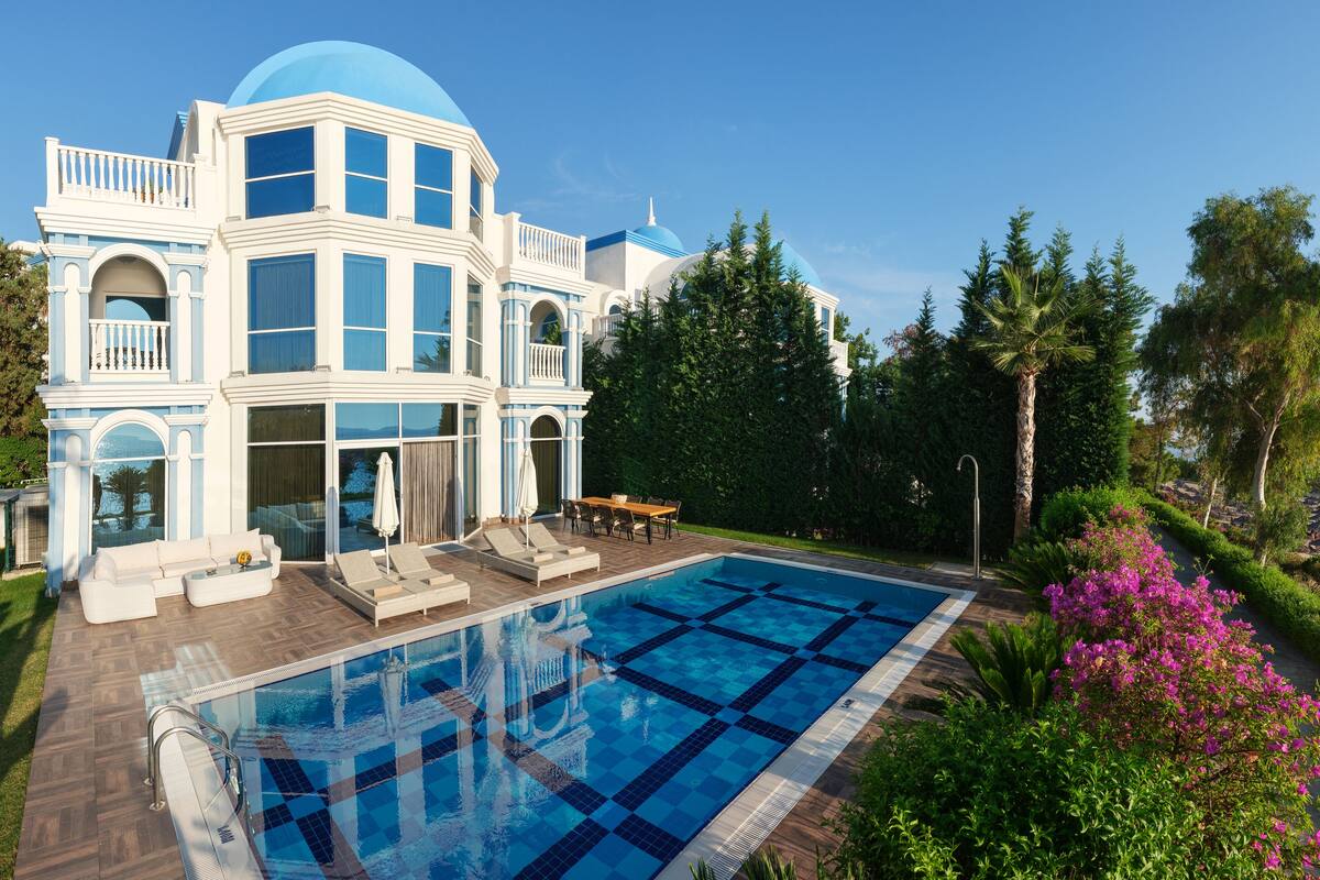 A large, modern house with a swimming pool, outdoor furniture, and lush greenery.