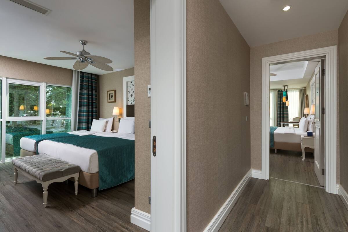 A hotel room with a bed, a bench, a ceiling fan, and a view of the outdoors through a window.