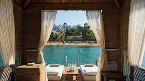 A wooden deck with two beds and a table, overlooking a beach and water. - Rubi Platinum Spa Resort & Suites - All Inclusive (Alanya)