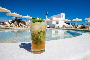 A glass of iced drink with mint leaves on a poolside table, surrounded by lounge chairs and umbrellas. - Evdokia (Naxos)