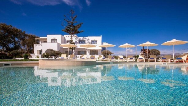 A clear swimming pool with lounge chairs and umbrellas, a white building with a modern design, and a clear blue sky. - Evdokia (Naxos)