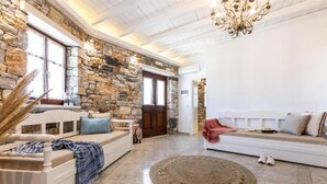 A cozy living room with a stone wall, a white sofa, a wooden bench, and a round rug. - Evdokia (Naxos)