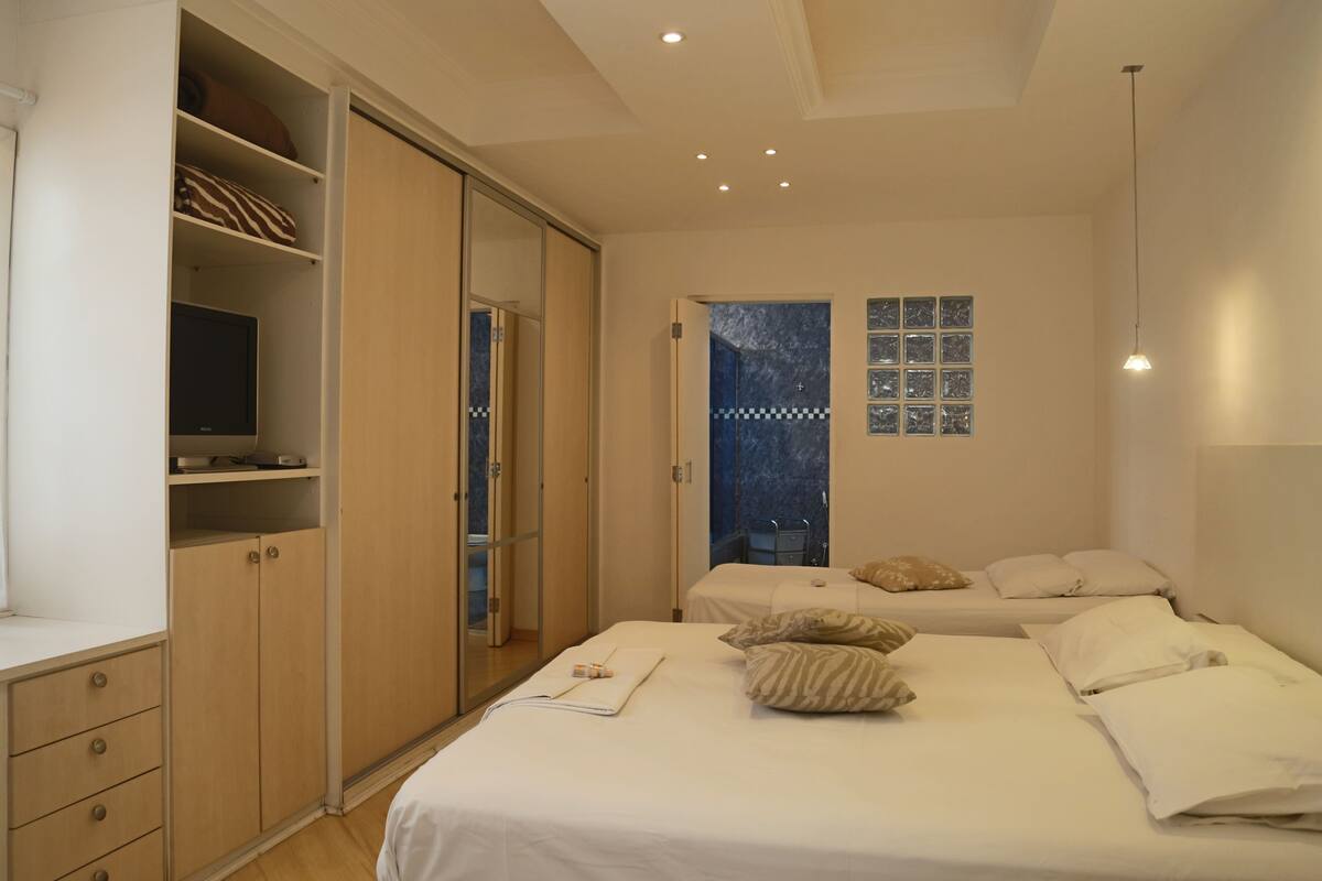 A bedroom with a large bed, a wardrobe, a television, and a shower area.