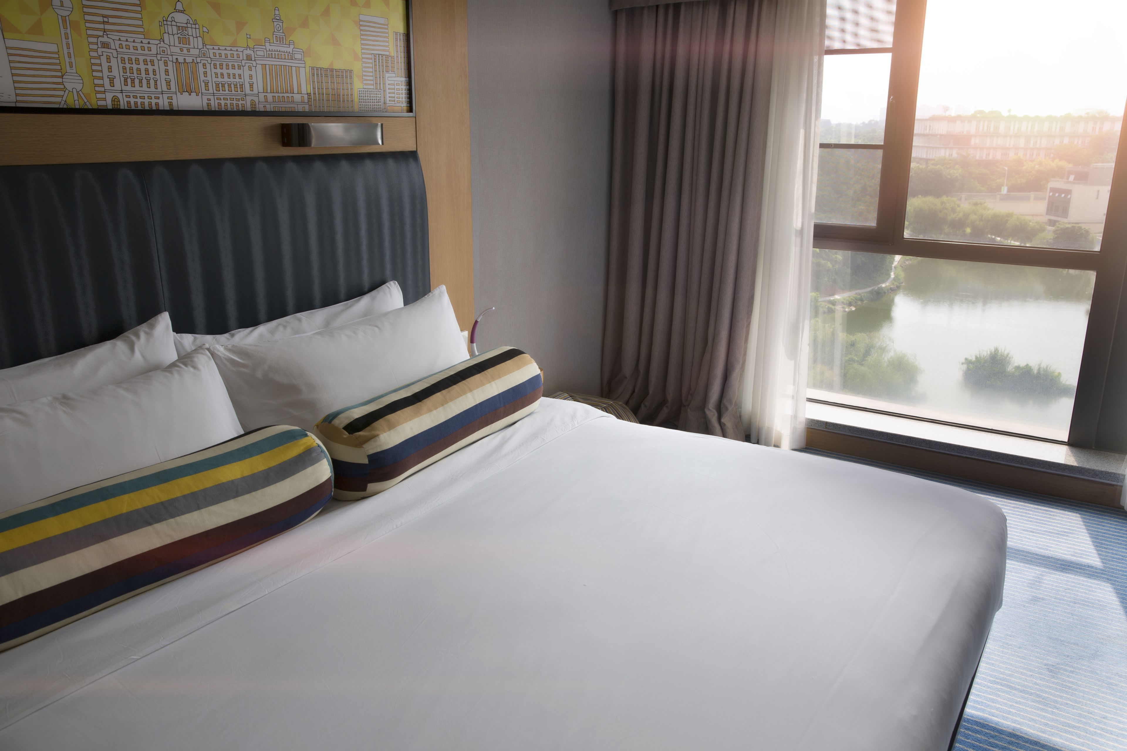 Ein Hotelzimmer mit einem großen Bett, einem Stadtbildgemälde an der Wand und Blick auf einen Fluss durch das Fenster.