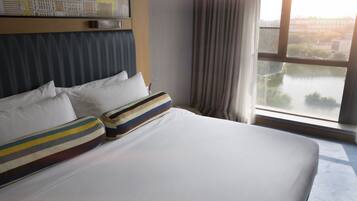 A hotel room with a large bed, a cityscape painting on the wall, and a view of a river through the window.