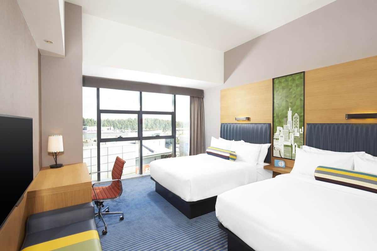 Hotelkamer met twee bedden, een bureau, een stoel, een televisie en een groot raam met uitzicht op de stad.