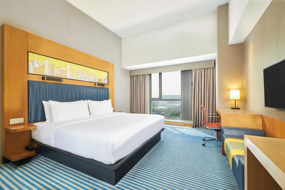 Hotelkamer met een groot bed, bureau, stoel, televisie en een stadsgezicht op de muur.