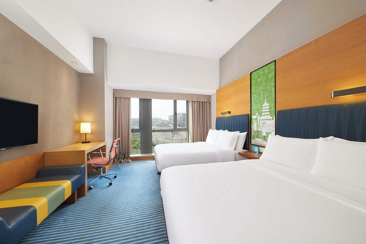 Een hotelkamer met twee bedden, een bureau, een televisie en uitzicht op de stad.