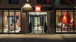 A hotel entrance with glass doors, a sign reading 'ibis HOTELS MÜNCHEN OST,' and a red sign above the entrance. - Ibis Muenchen City Ost (Munich)