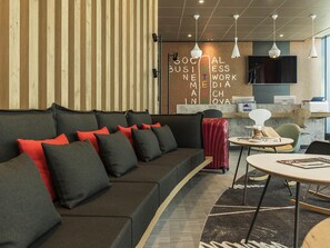 A modern lounge area with a curved sofa, a small round table, and a reception desk. - Ibis Muenchen City Ost (Munich)