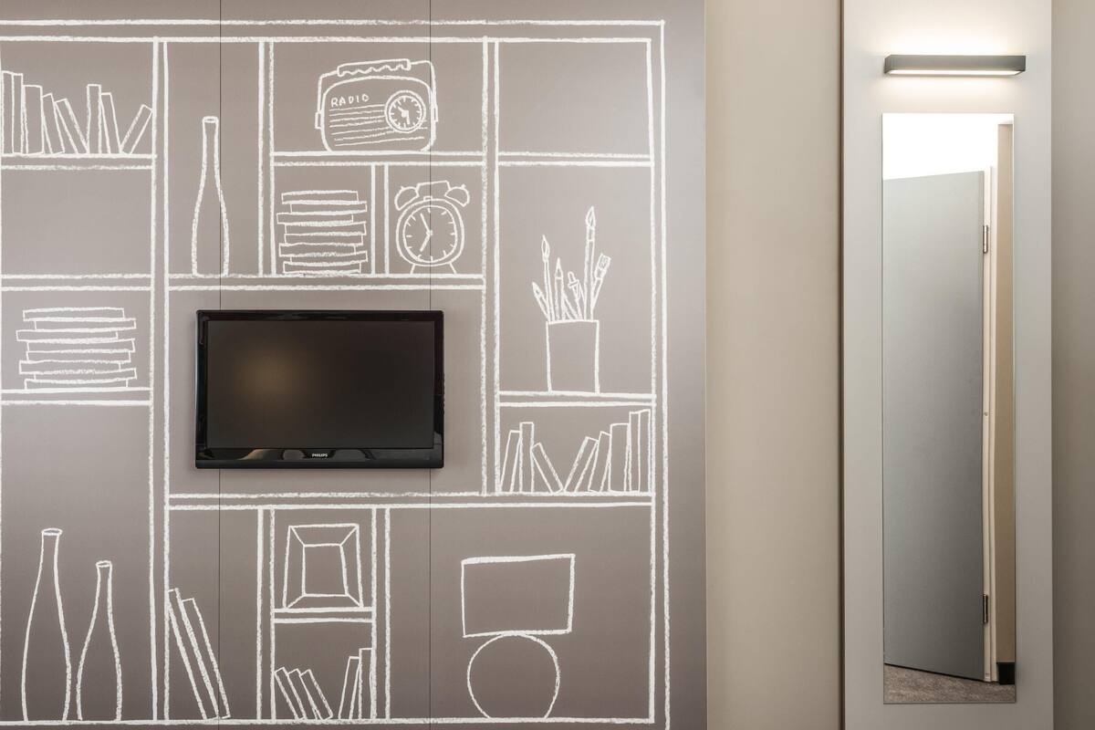 A wall with a flat-screen TV mounted above a chalkboard-style wall art depicting various objects like books, a radio, and a clock.