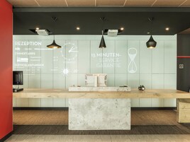 Una reception con uno schermo digitale, illuminazione a sospensione e un bancone in marmo.