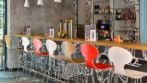 A bar area with modern chairs, a counter, and a wall with abstract designs. - Ibis Muenchen City Ost (Munich)