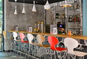 Un'area bar con sedie moderne, un bancone e una parete con motivi astratti.