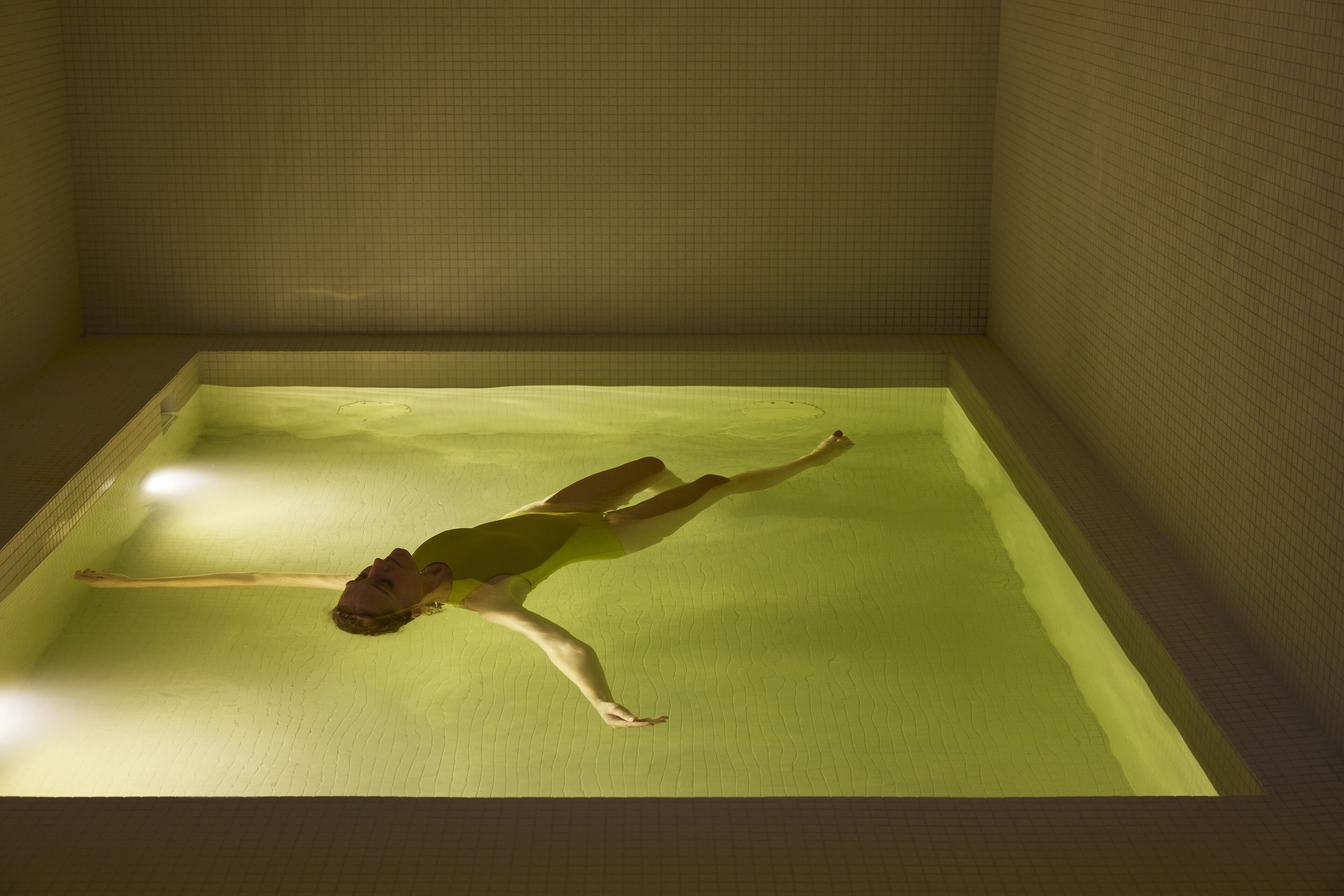 A person floating in a rectangular pool with tiled walls.