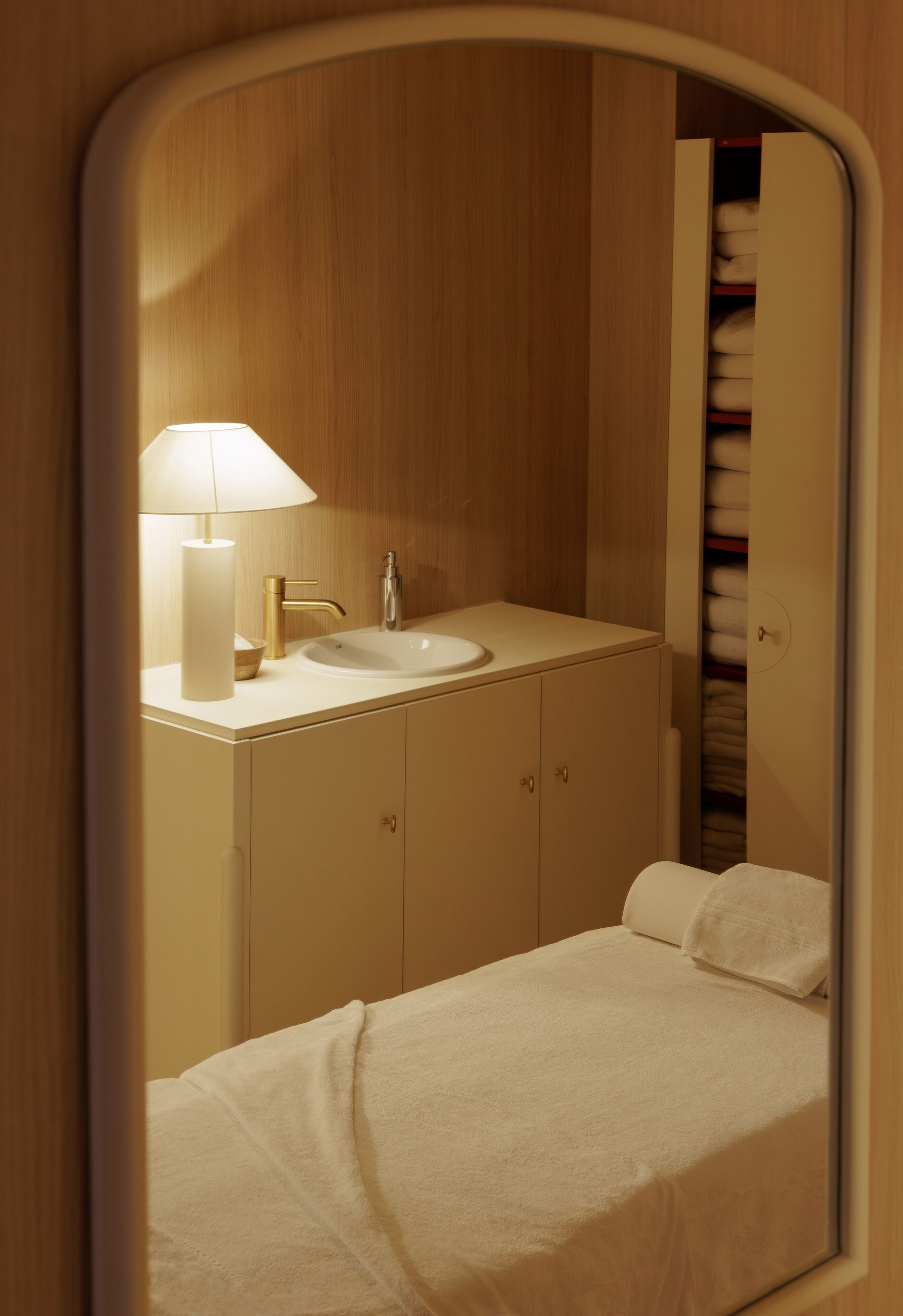 A small, compact bedroom with a single bed, a bedside table, a lamp, and a mirror.