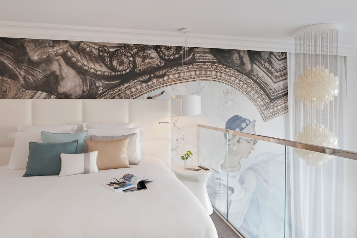 Une chambre d’hôtel moderne avec un grand lit, une cloison en verre et une fresque murale.