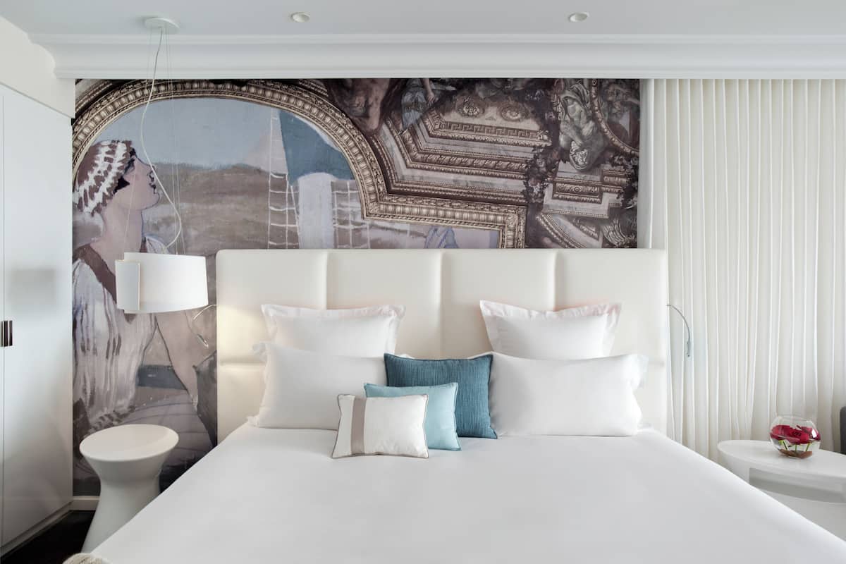 Une chambre d’hôtel moderne avec un grand lit, du linge de lit blanc et une fresque murale décorative.