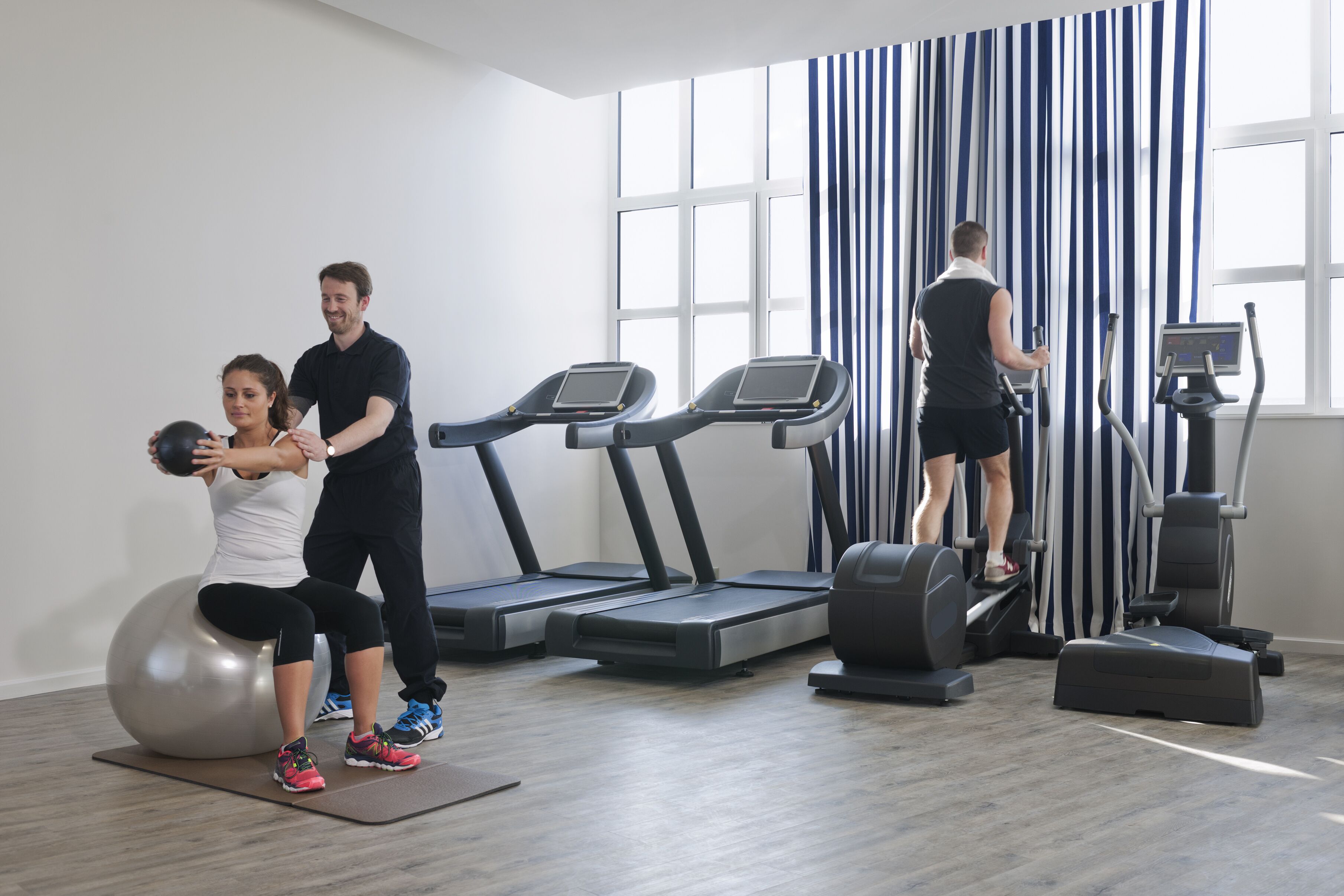 Een sportschool met loopbanden, een fitnessbal en een roeimachine.